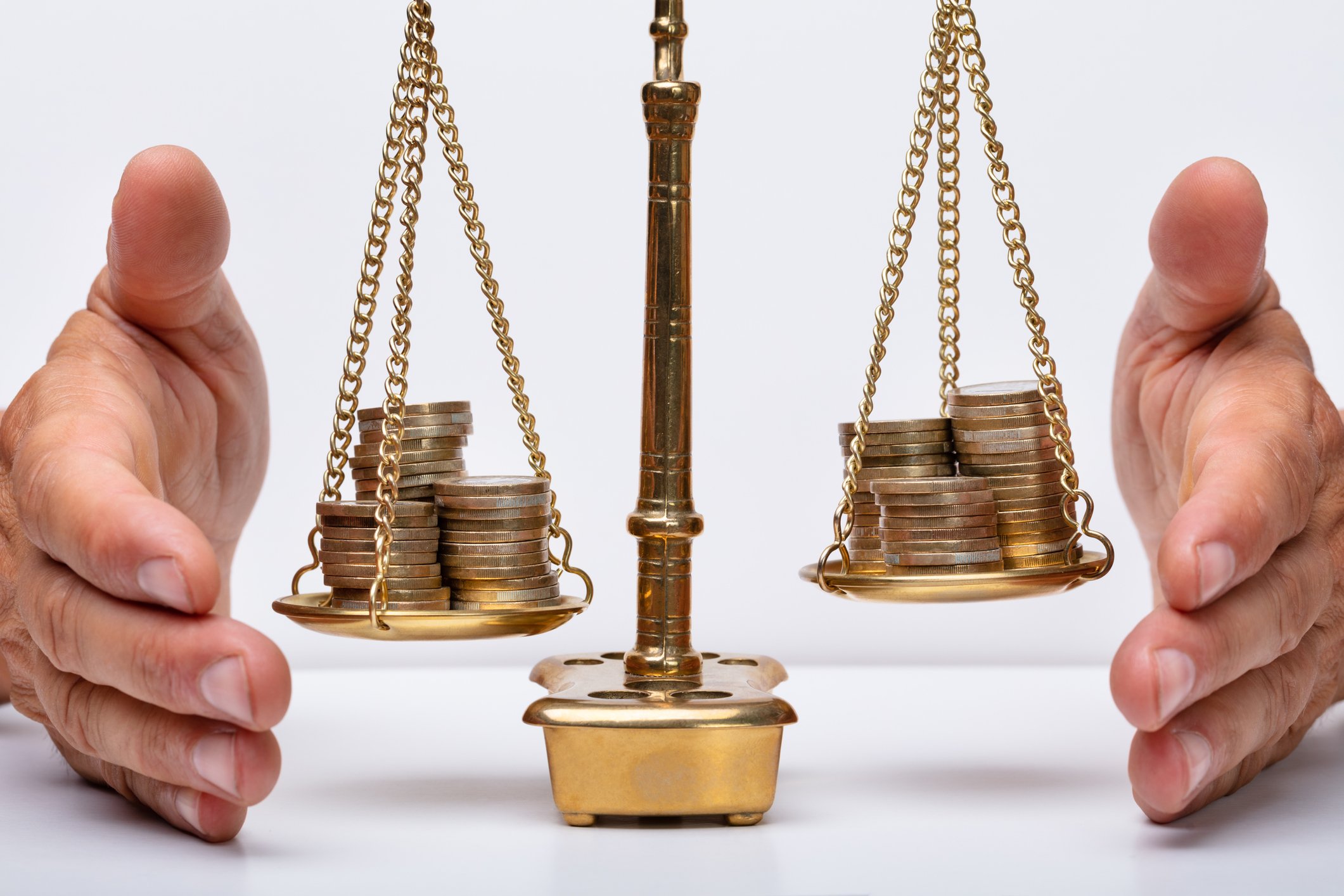 A man's hands on either side of a balance scale weighing stacks of coins.