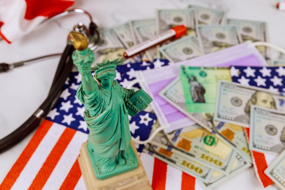 Statue of liberty model on top of American flag, next to dollar bills.