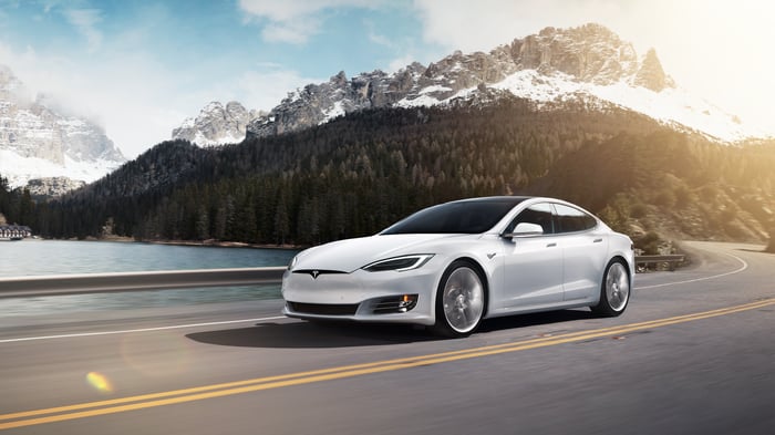 A white Tesla Model S cruising by a snowy mountain. 