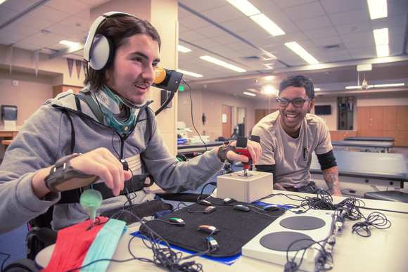 Gamer Testing an Xbox Adaptive Controller, while a friend looks on.