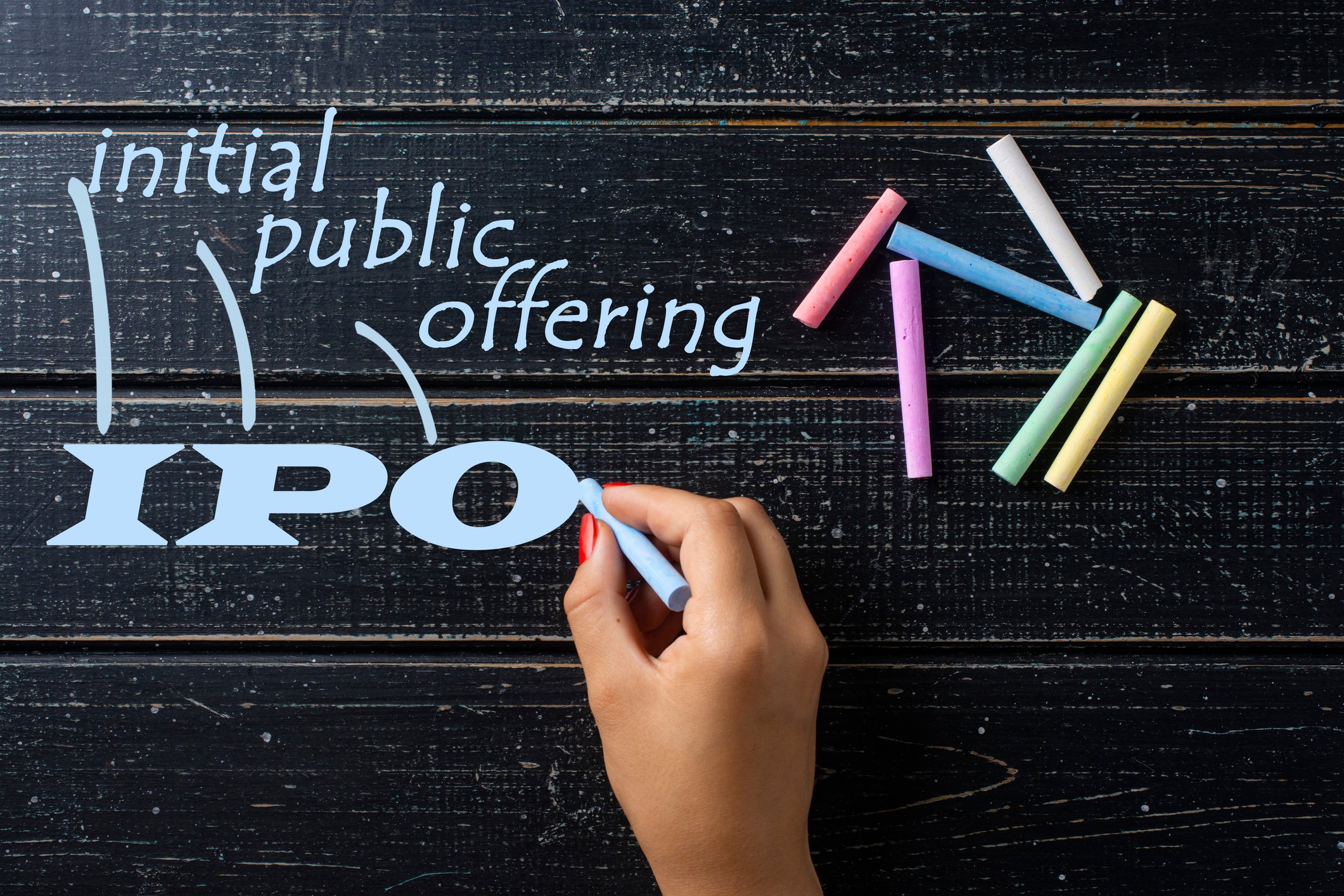 A hand draws “IPO” with a piece of blue chalk.