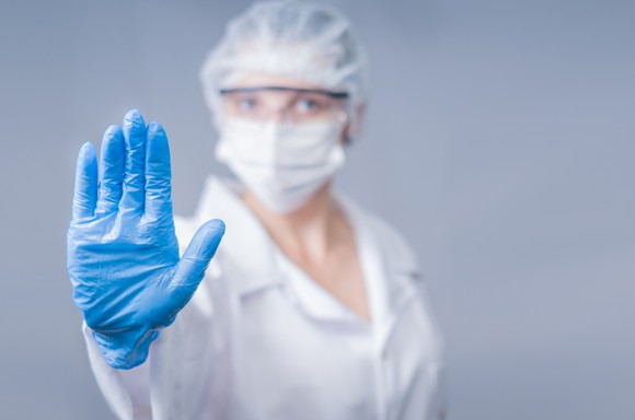 Healthcare provider in personal protective gear holding out hand in a stop gesture.