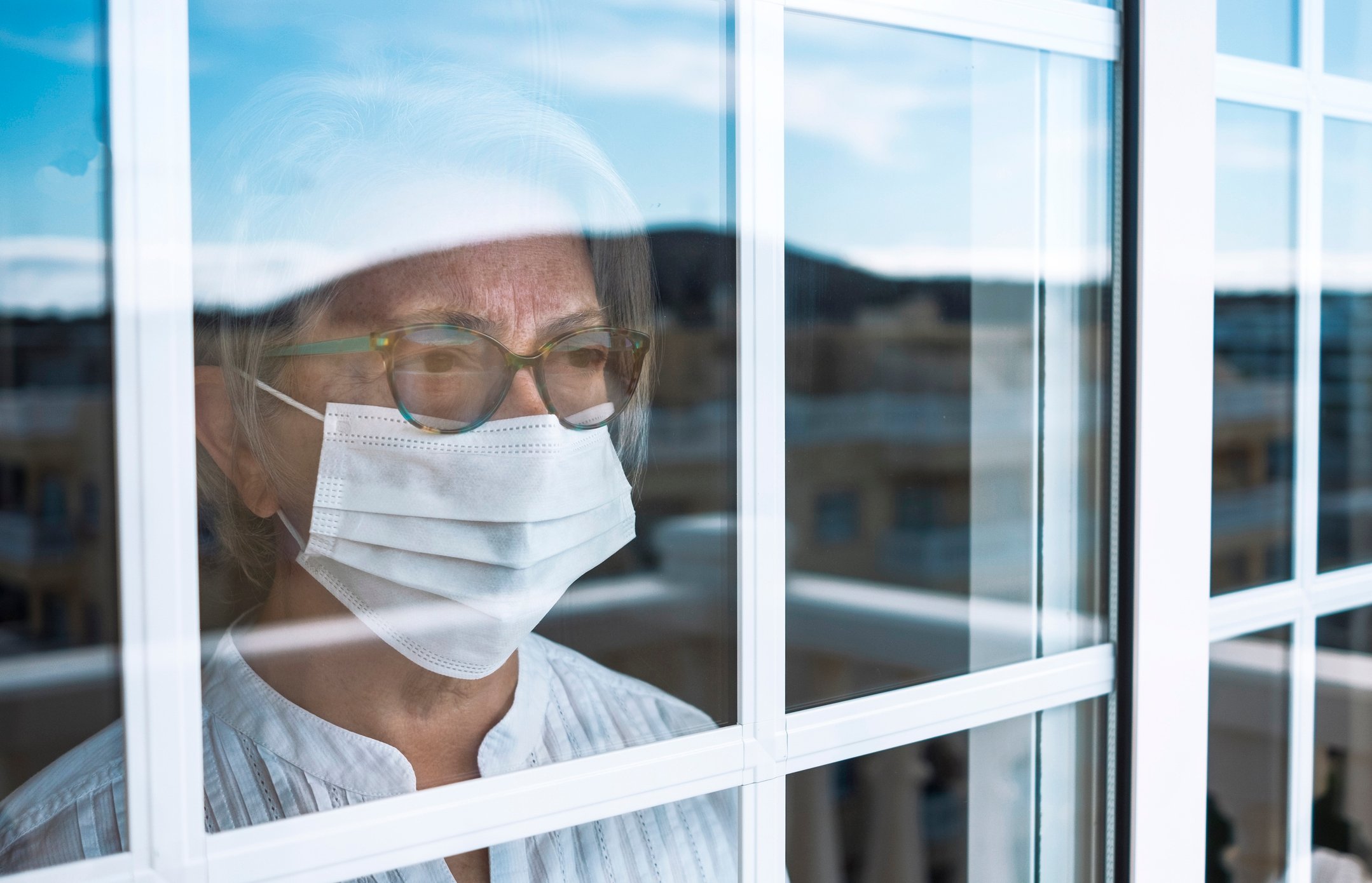 A retiree wearing a mask gazing out a window