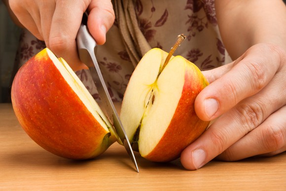 An apple getting sliced in half on a table.