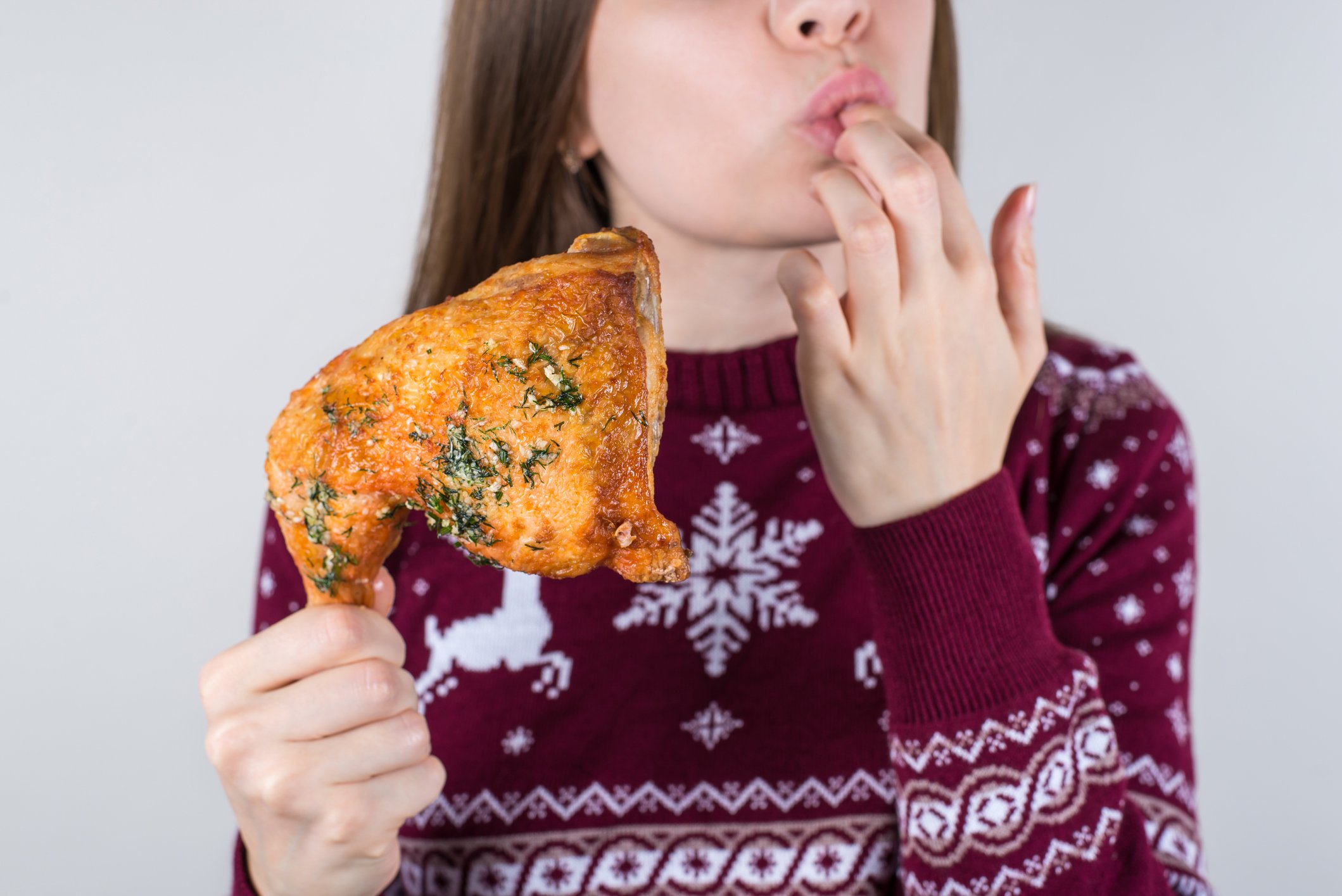 Woman holding piece of chicken licking her fingers