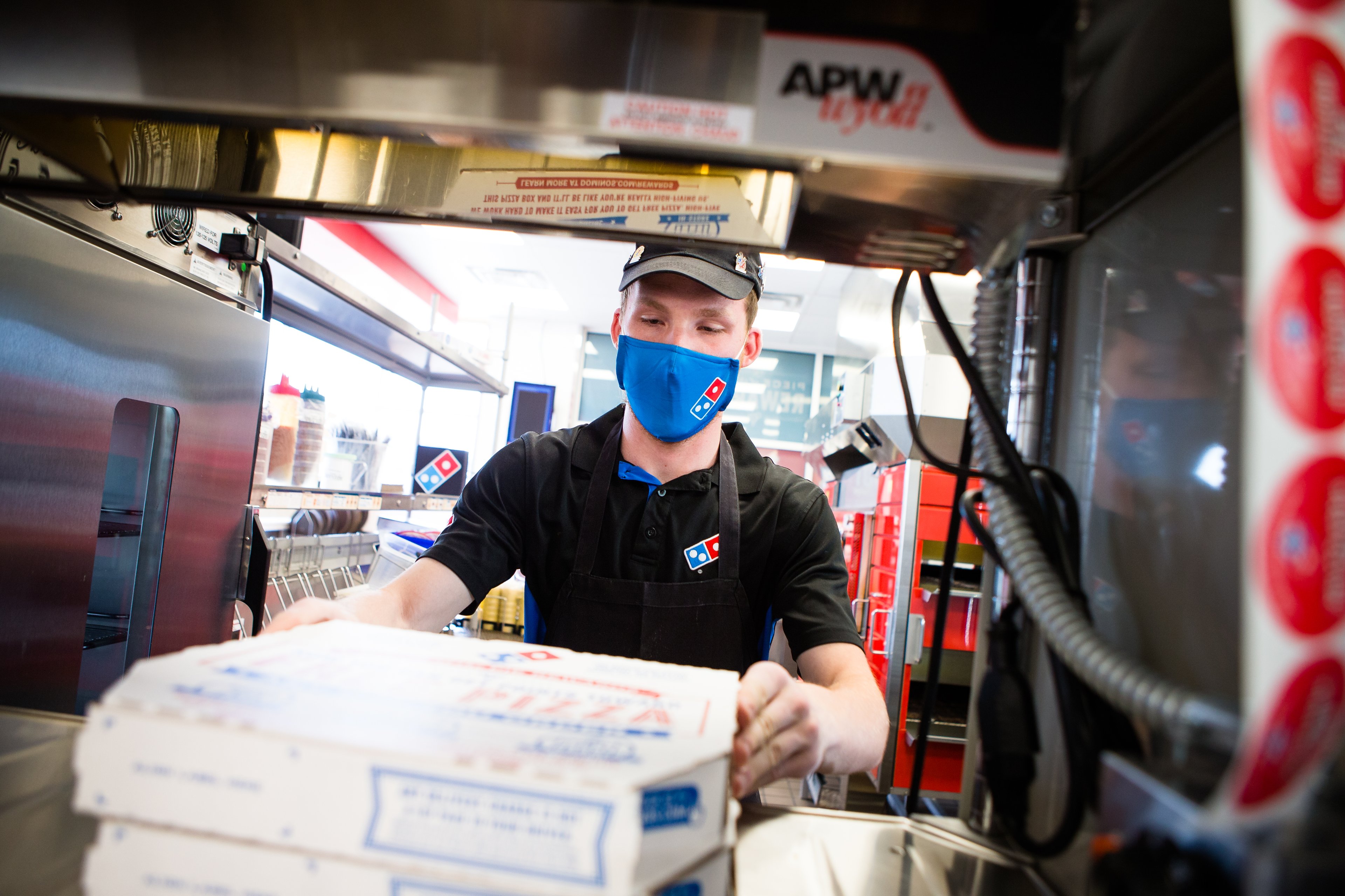 Domino's Pizza worker wearing mask with stack of pizzas
