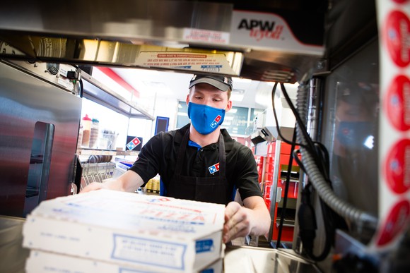 Domino's Pizza worker wearing mask with stack of pizzas