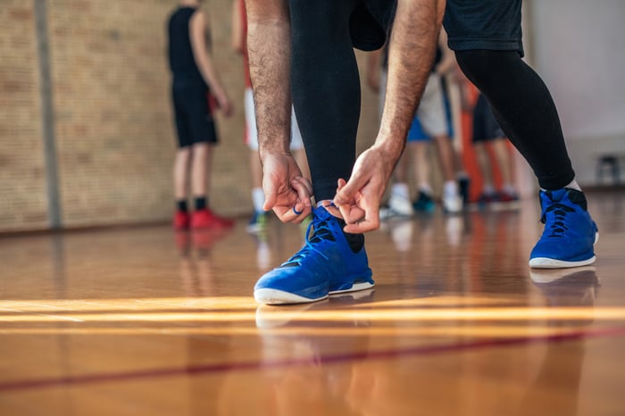 Man tying shoelaces of his basketball shoes on court.