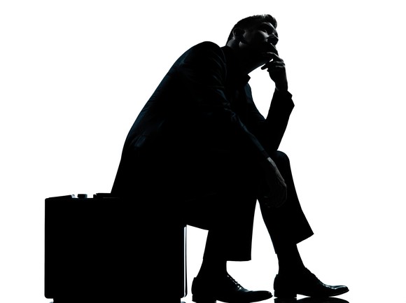 A businessman sits on his briefcase in deep thought.