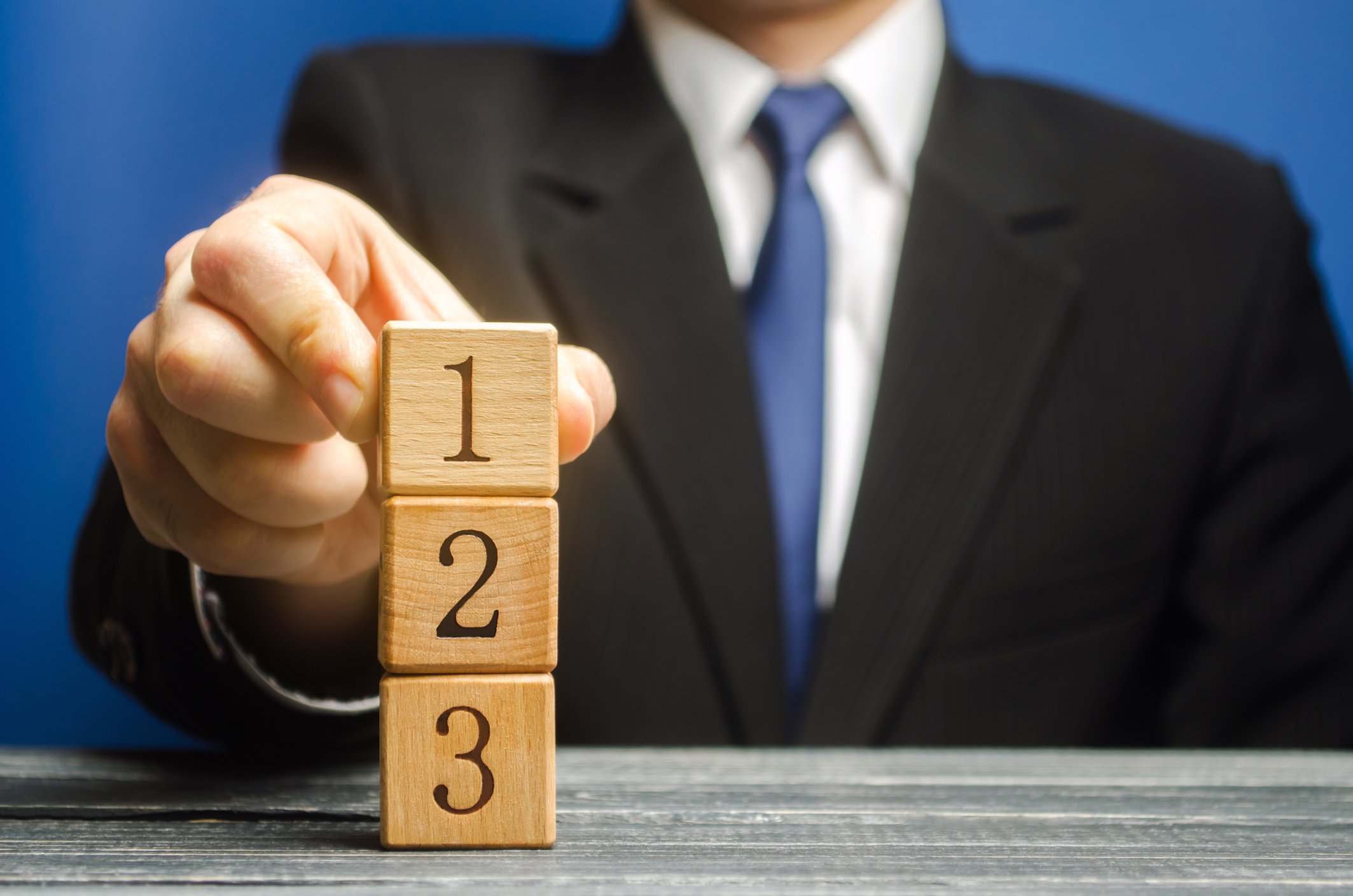 Man in suit stacking numbered wooden blocks on a desk.
