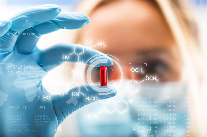 A scientist looks at a red medicine capsule