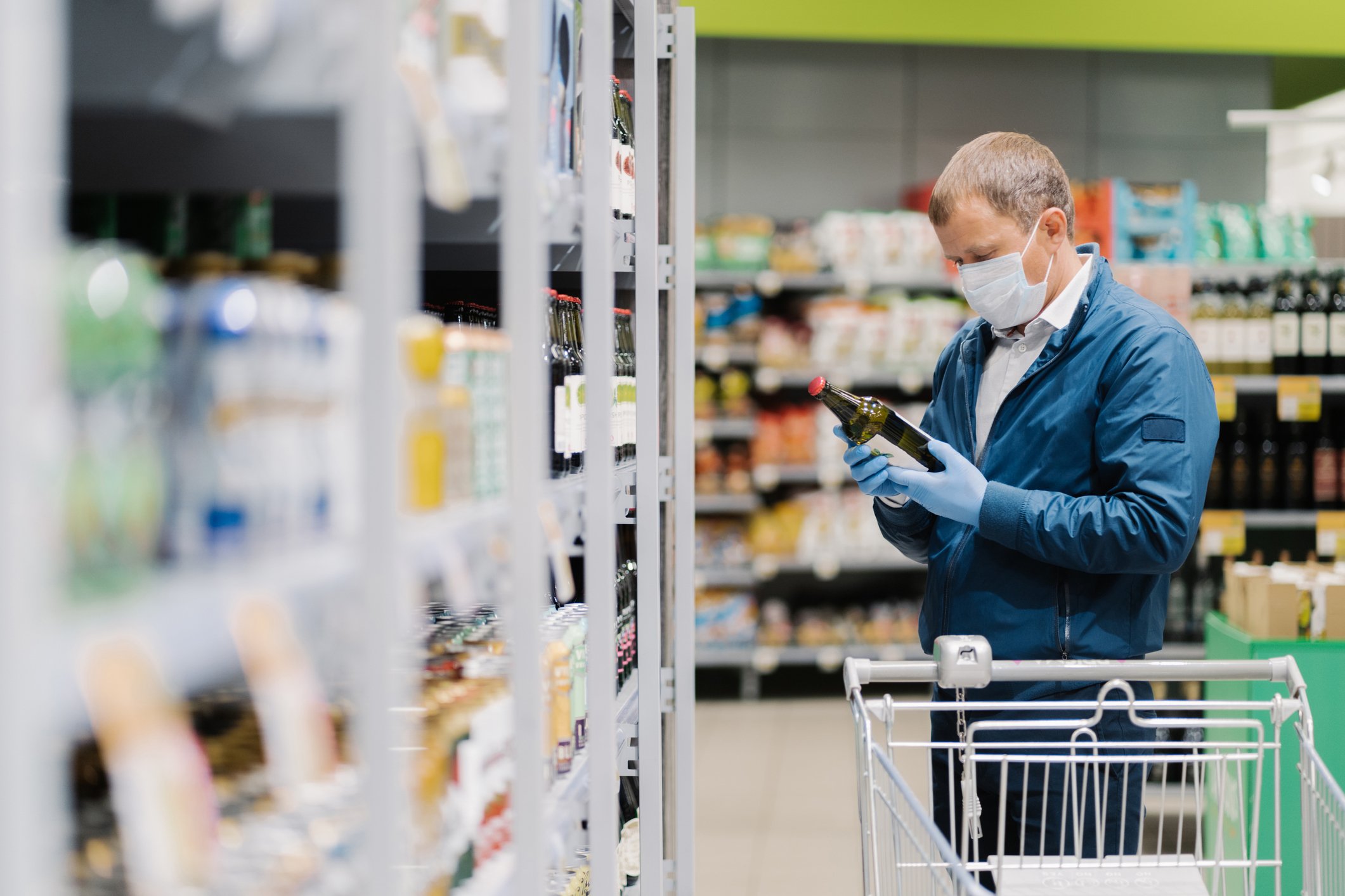 A man wearing a mask and gloves holding a bottle in a food store.