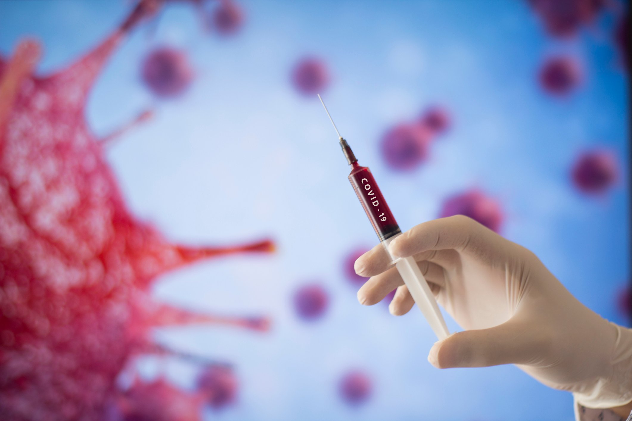 A gloved hand readies a syringe labeled COVID-19