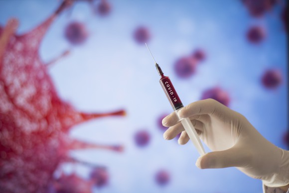 A gloved hand readies a syringe labeled COVID-19
