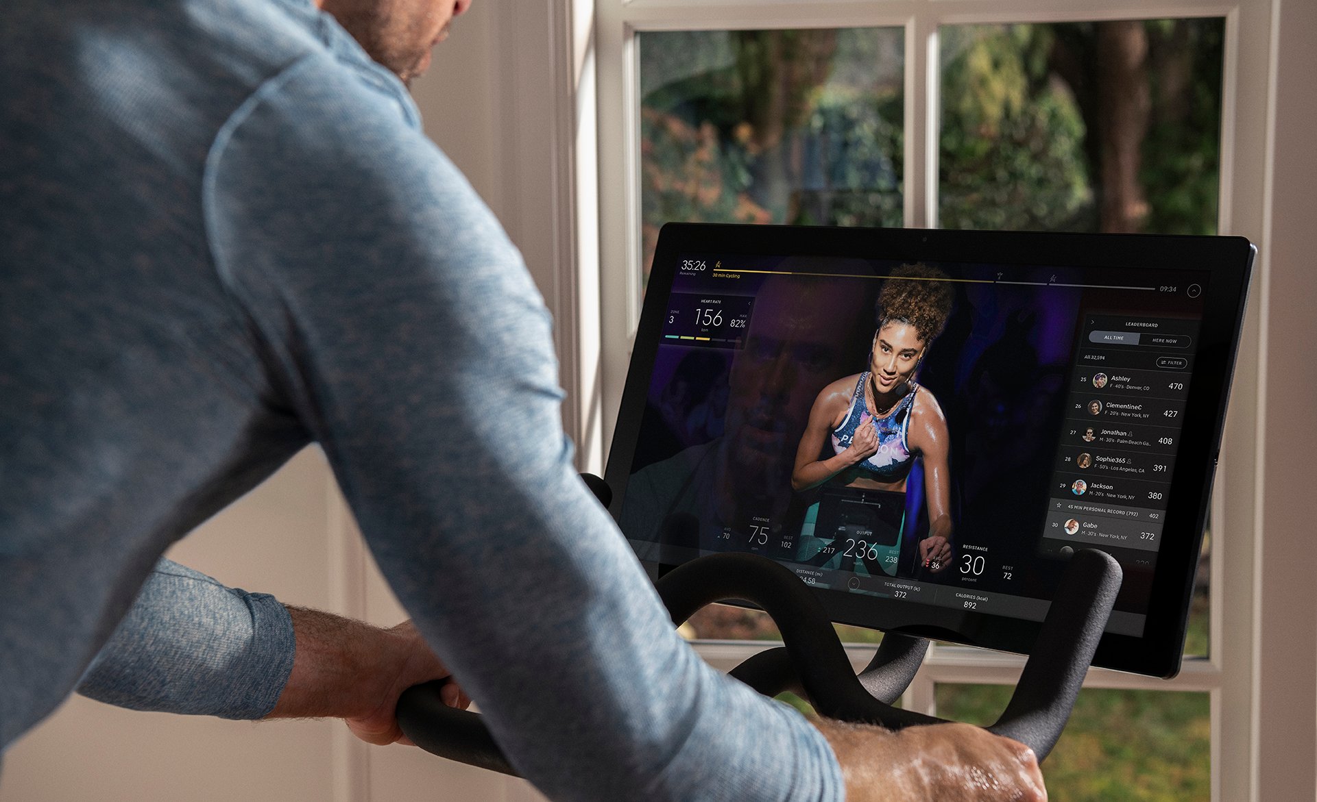 A person is exercising on a Peloton bike while watching a fitness class.