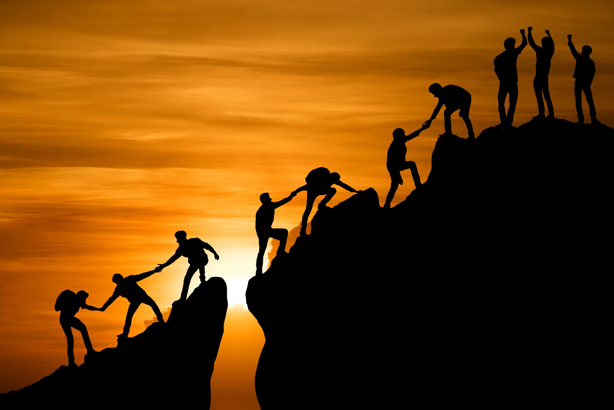 Silhouettes of people helping each other climb a mountain.