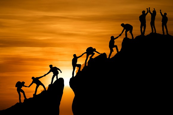 Silhouettes of people helping each other climb a mountain.