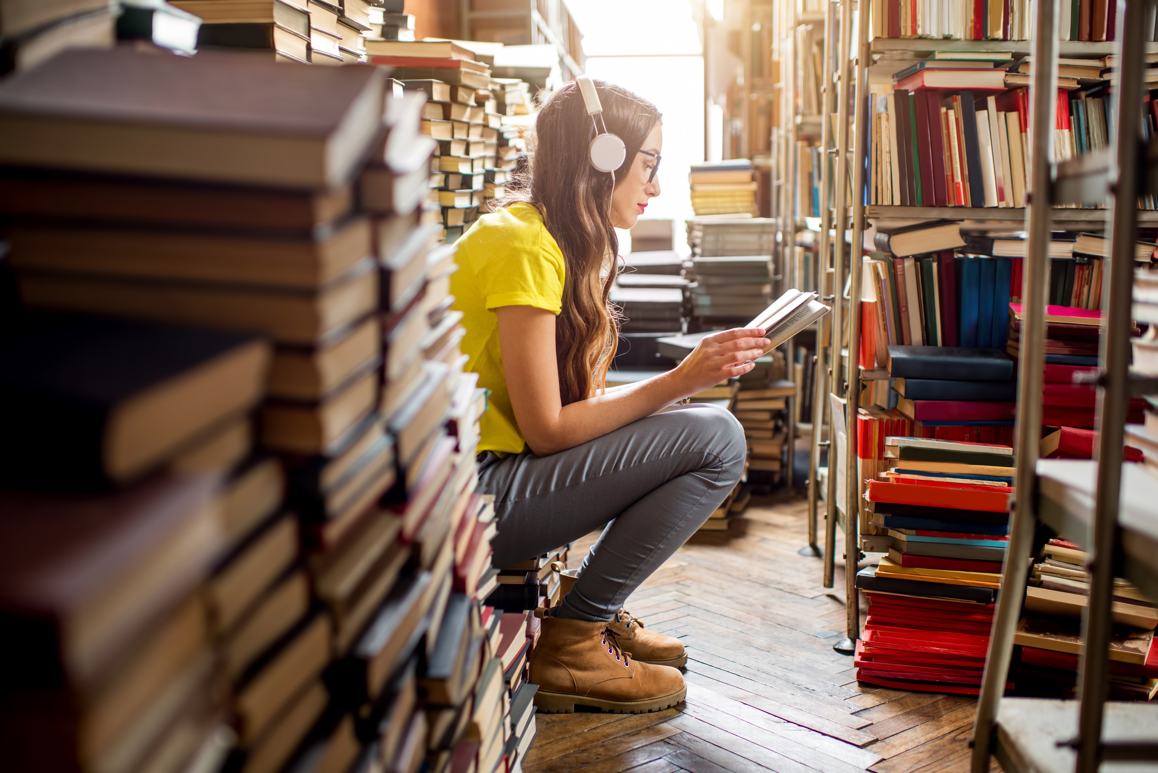 A young woman listens to music while reading in a library.