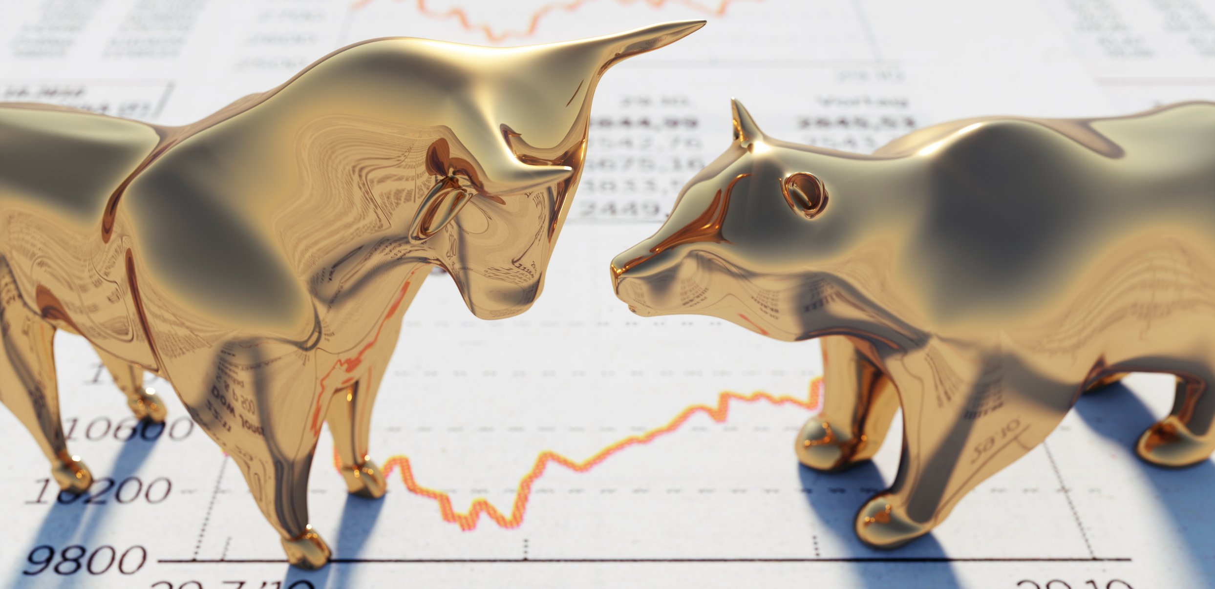 Bull and bear figurines standing on a newspaper page with stock quotes and charts on it.