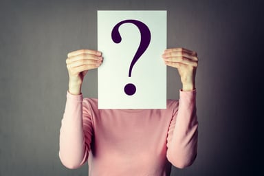 Woman holding question mark in front of face
