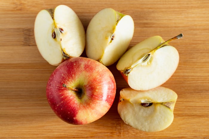 One whole apple is next to another apple that's cut into four slices.