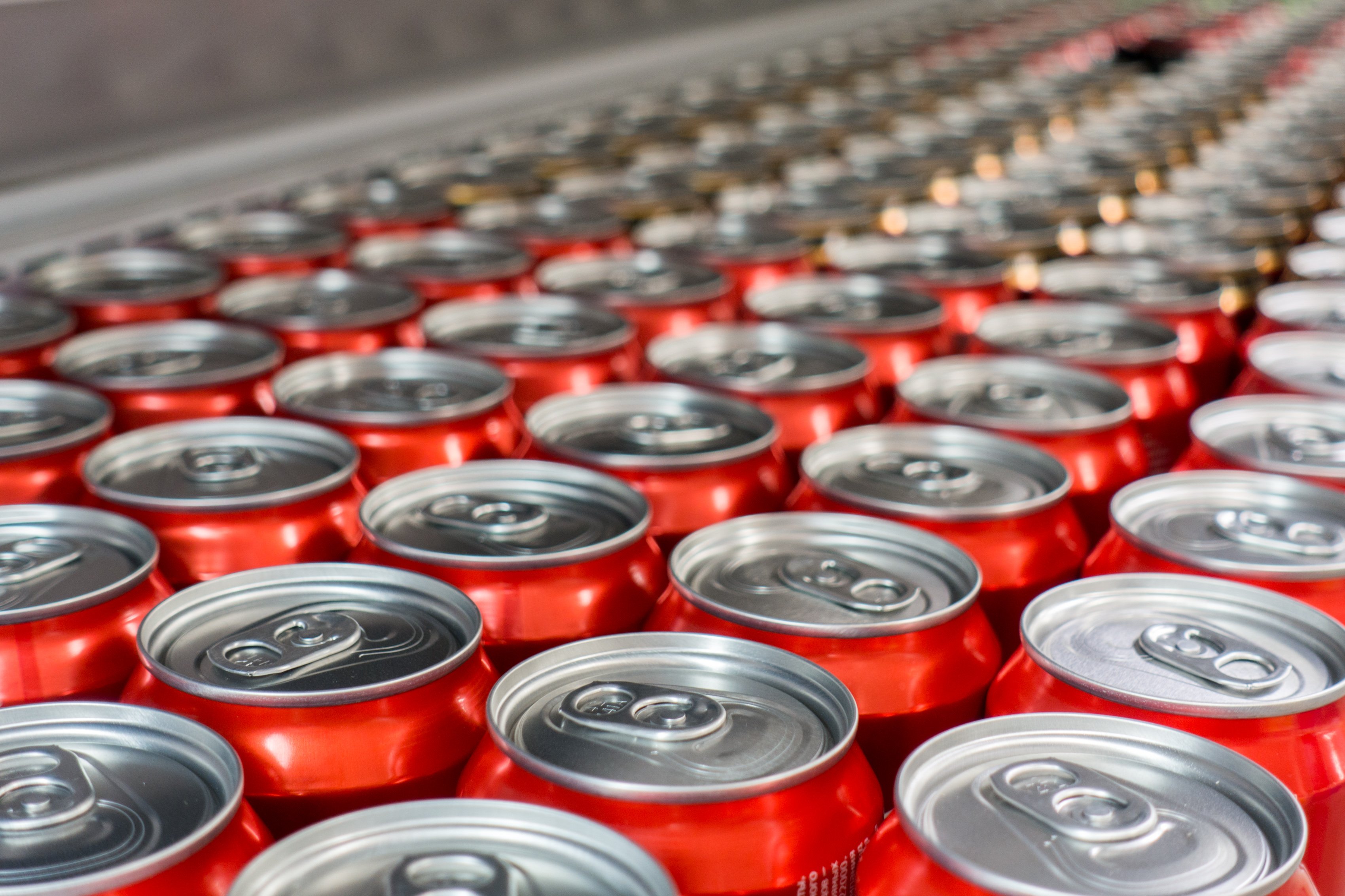 Rows of red aluminum soda cans seen from overhead in a manufacturing facility.