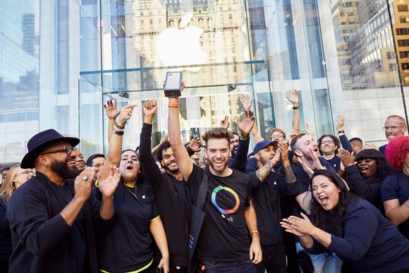 Apple employees cheering on a customer holding a new iPhone in front of an Apple store. 