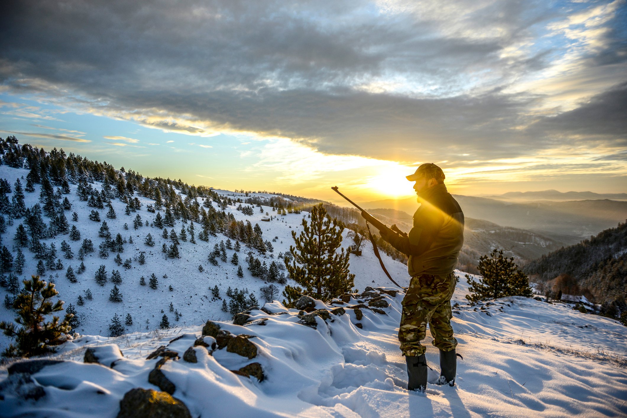 A man dressed for the outdoors holding a rifle on a snowy mountainside