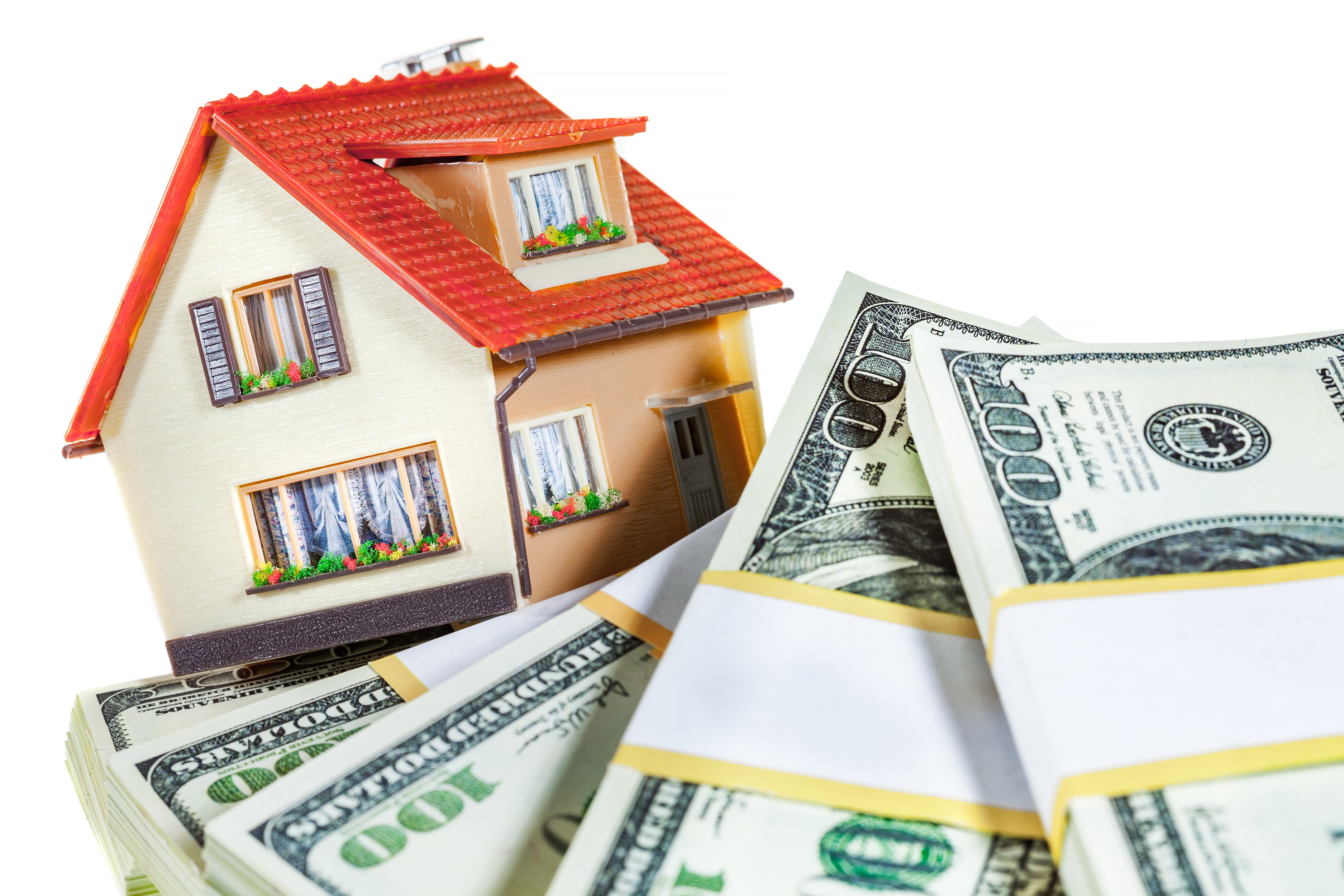 A small model house is atop some bundles of hundred dollar bills. 