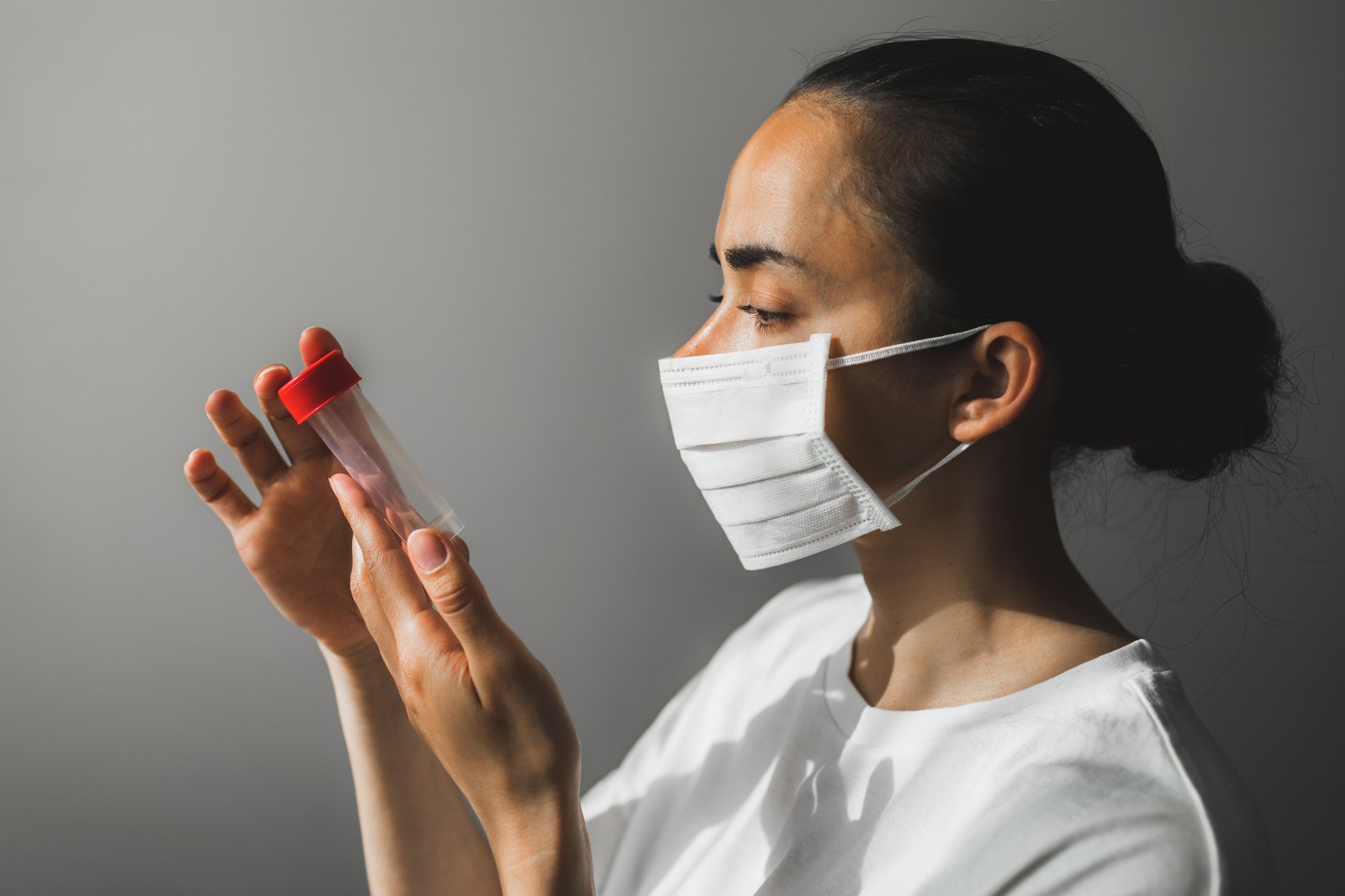 A woman in a medical mask looking at a test tube.