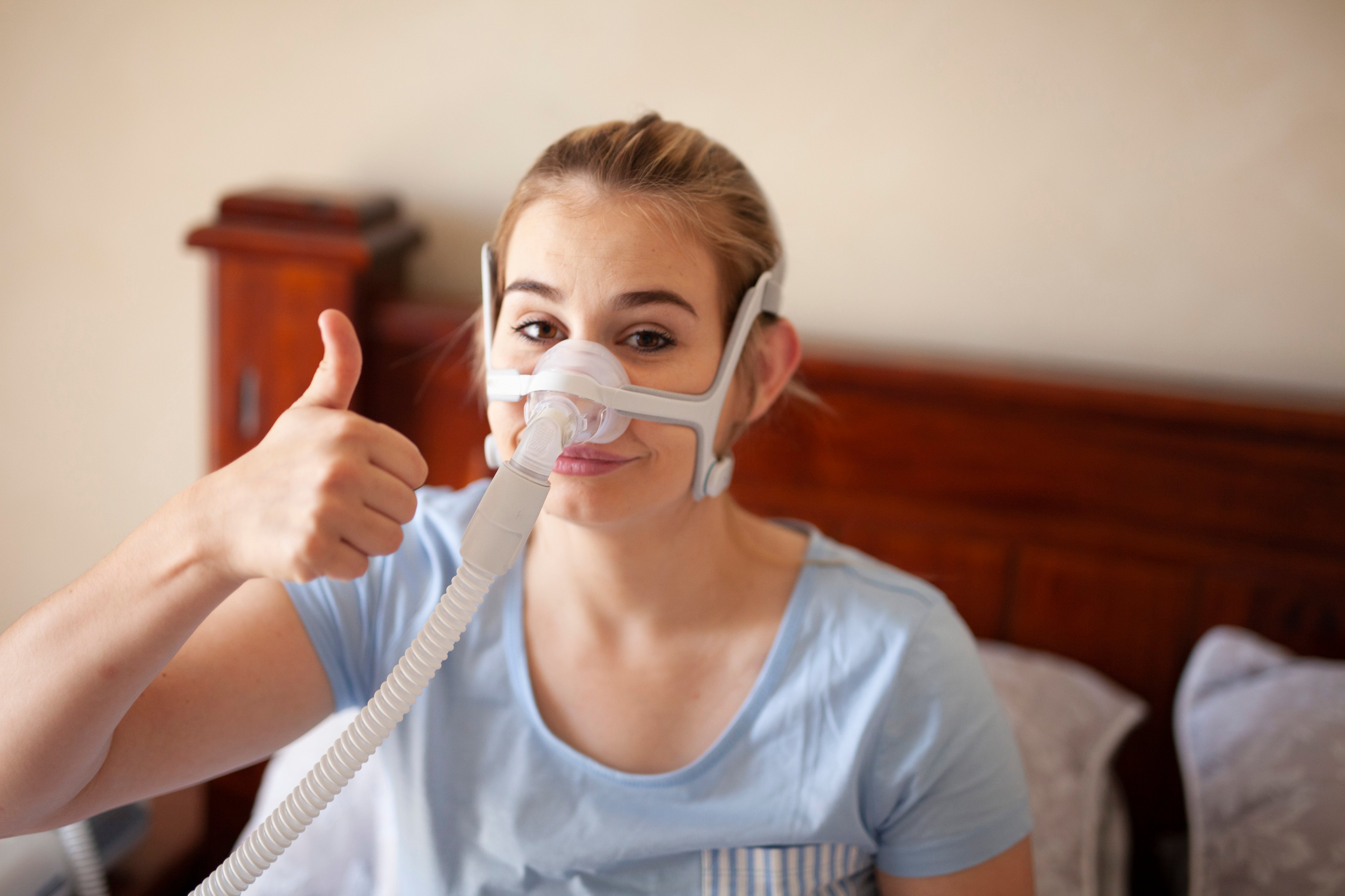 A woman with a CPAP device gives a thumbs up.