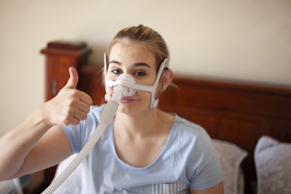 A woman with a CPAP device gives a thumbs up.