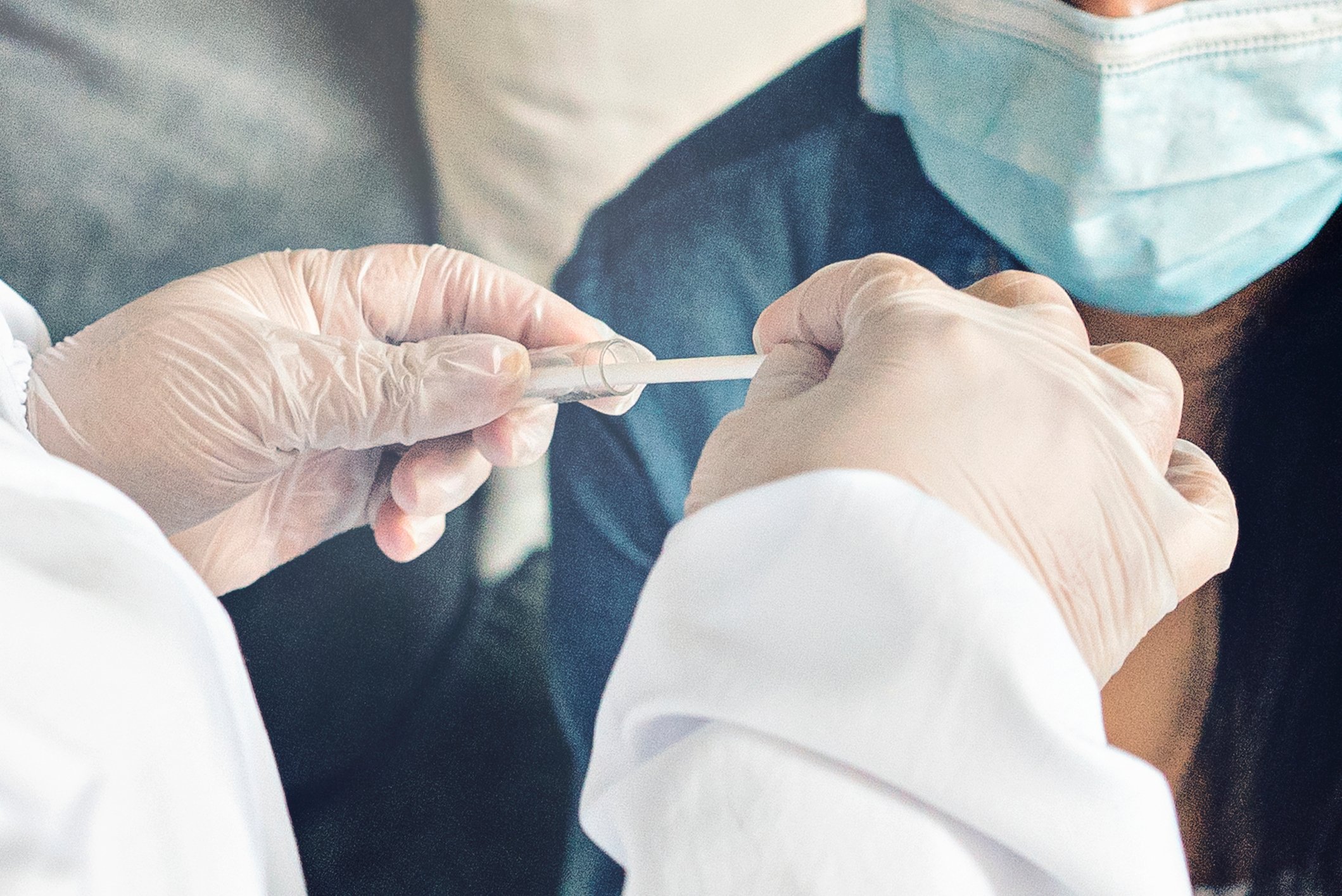 A gloved healthcare provider prepares a nasal swab for a patient wearing a mask.