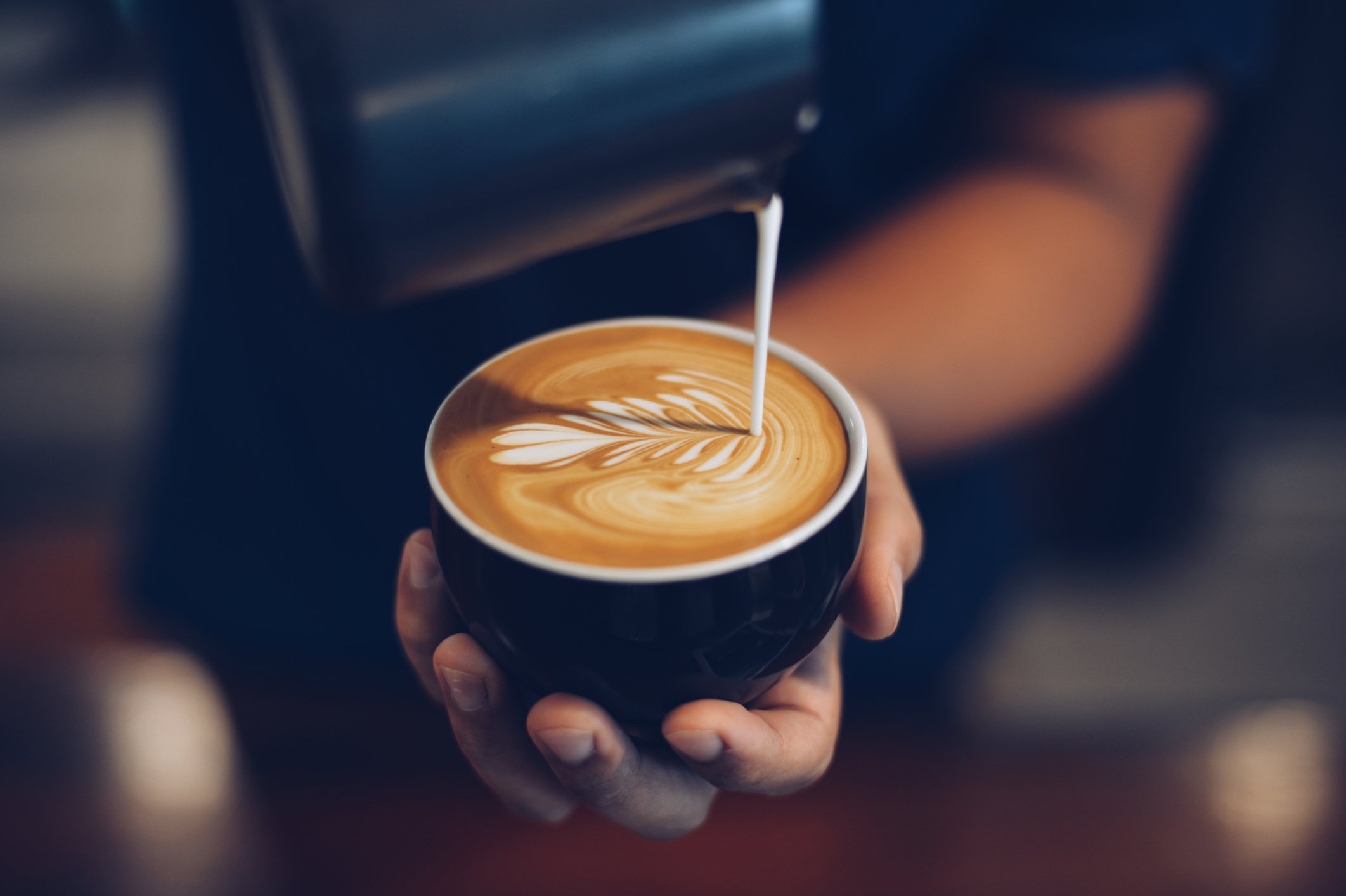 Person adding milk to a cup of coffee from a jug,