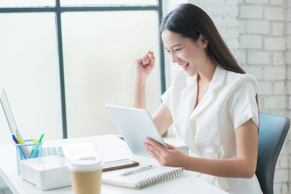 A woman smiles as she looks at her share holdings on her laptop.
