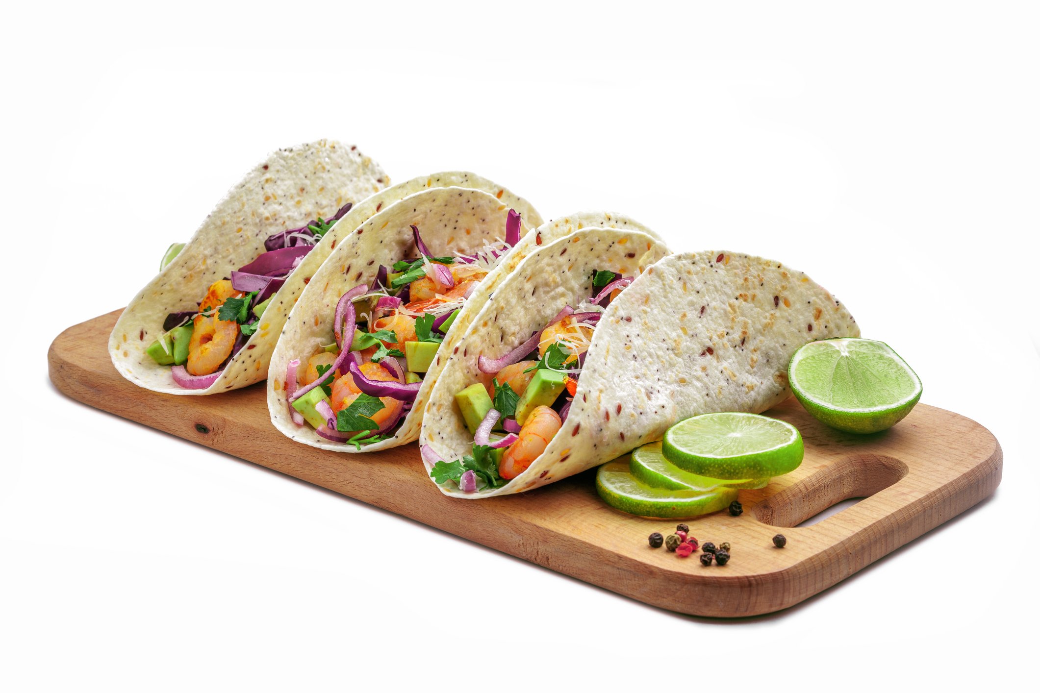 Three tacos sitting on a wooden board with lime beside them.