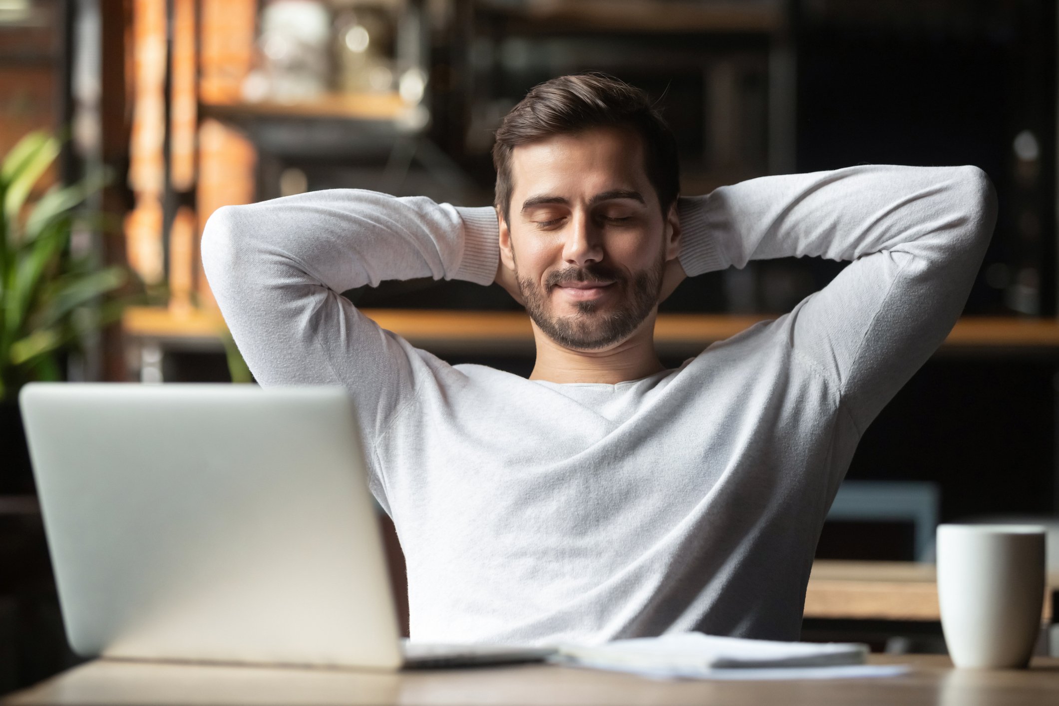 Relaxed happy man at desk meditating in front of laptop