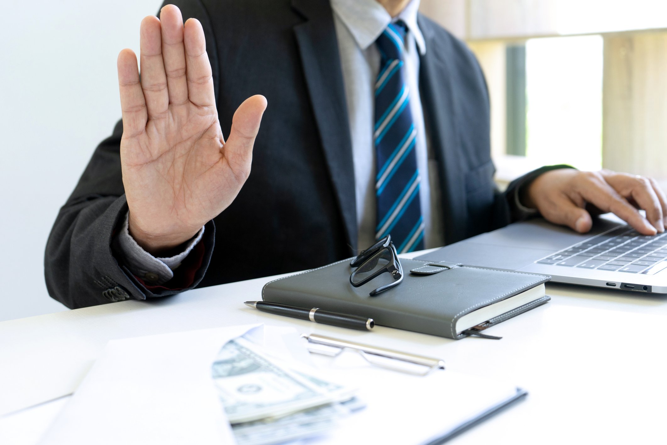A man in a business suit holds up the palm of his hand facing the viewer to indicate hesitation.