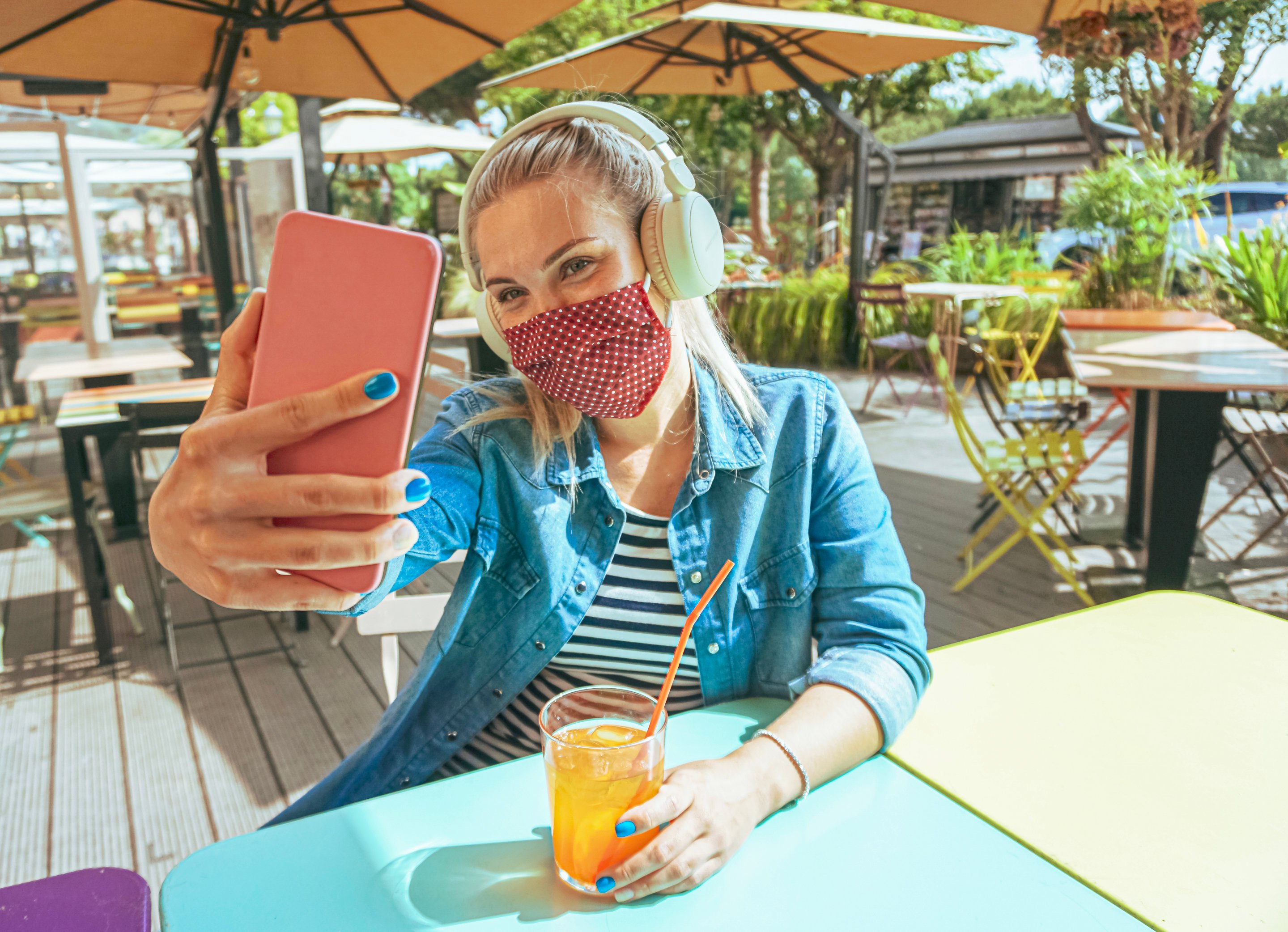 A young woman takes a selfie with her phone at an outdoor cafe. 