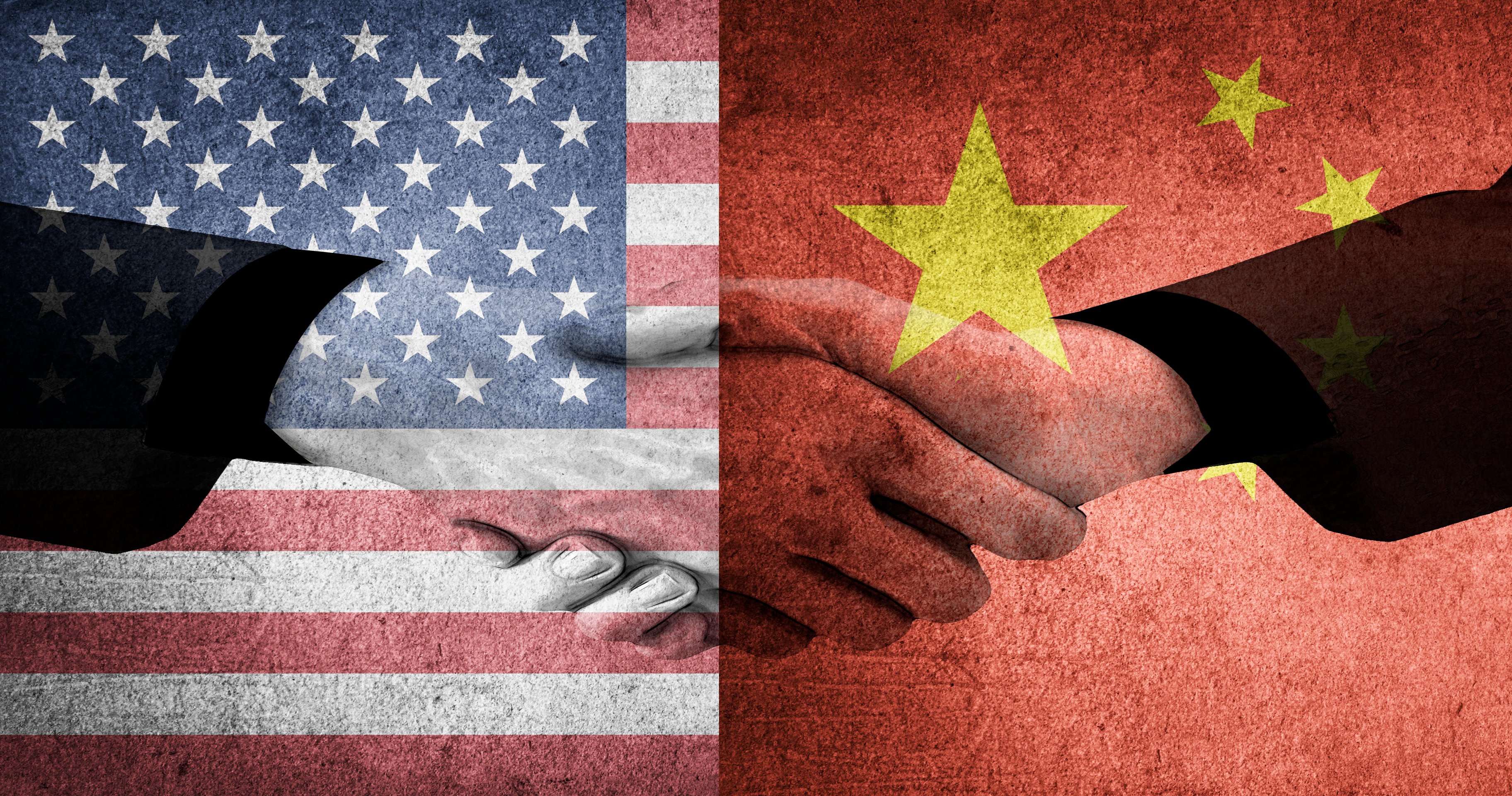 Two people are shaking hands against a backdrop of the U.S. and China's flags.