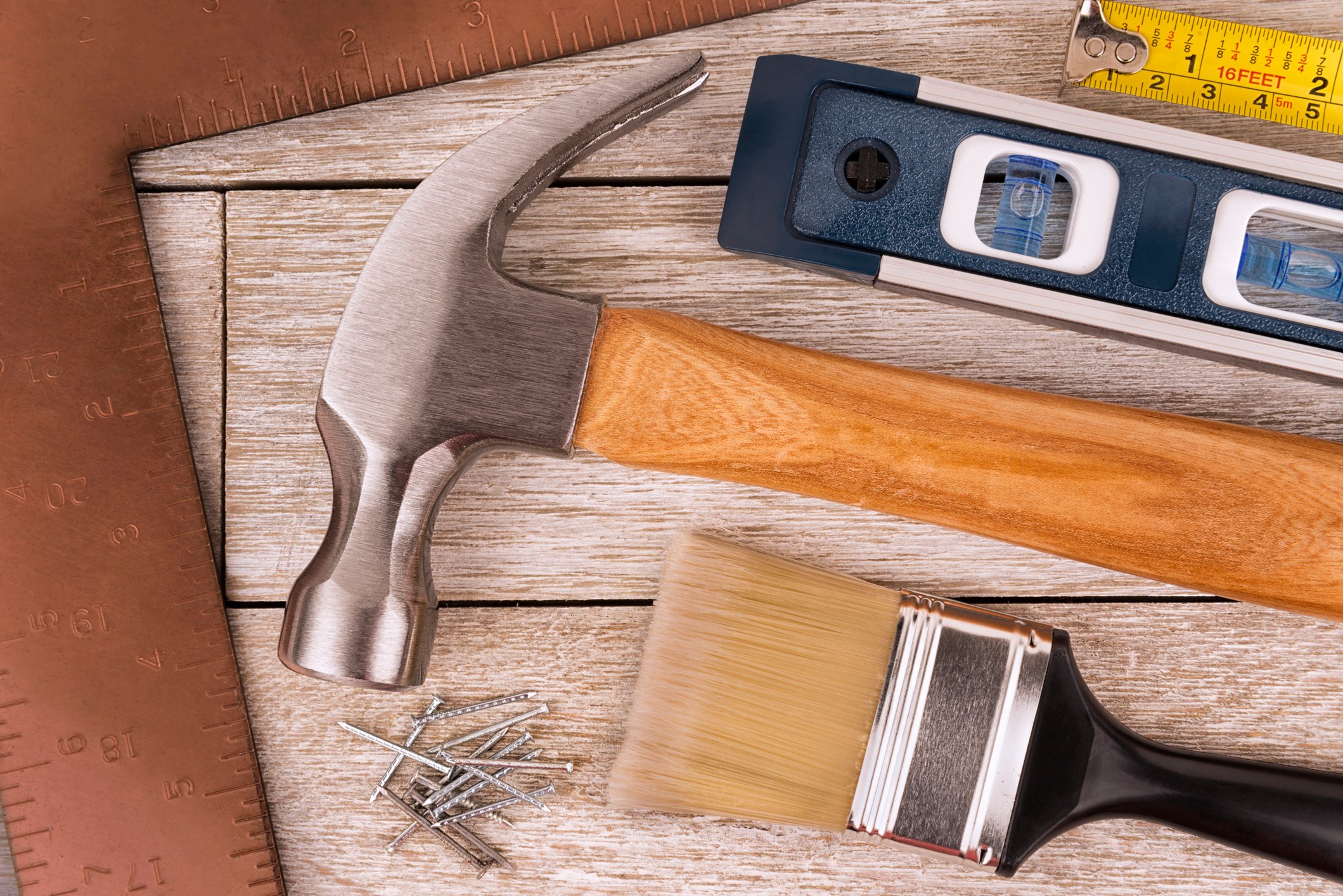 Closeup of ruler, level, hammer, paint brush, and nails.