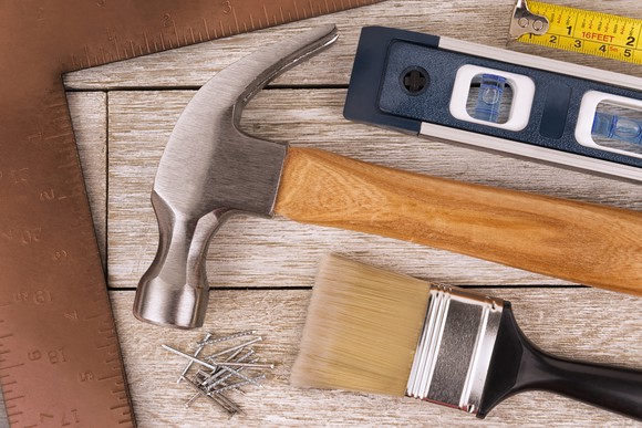 Closeup of ruler, level, hammer, paint brush, and nails.