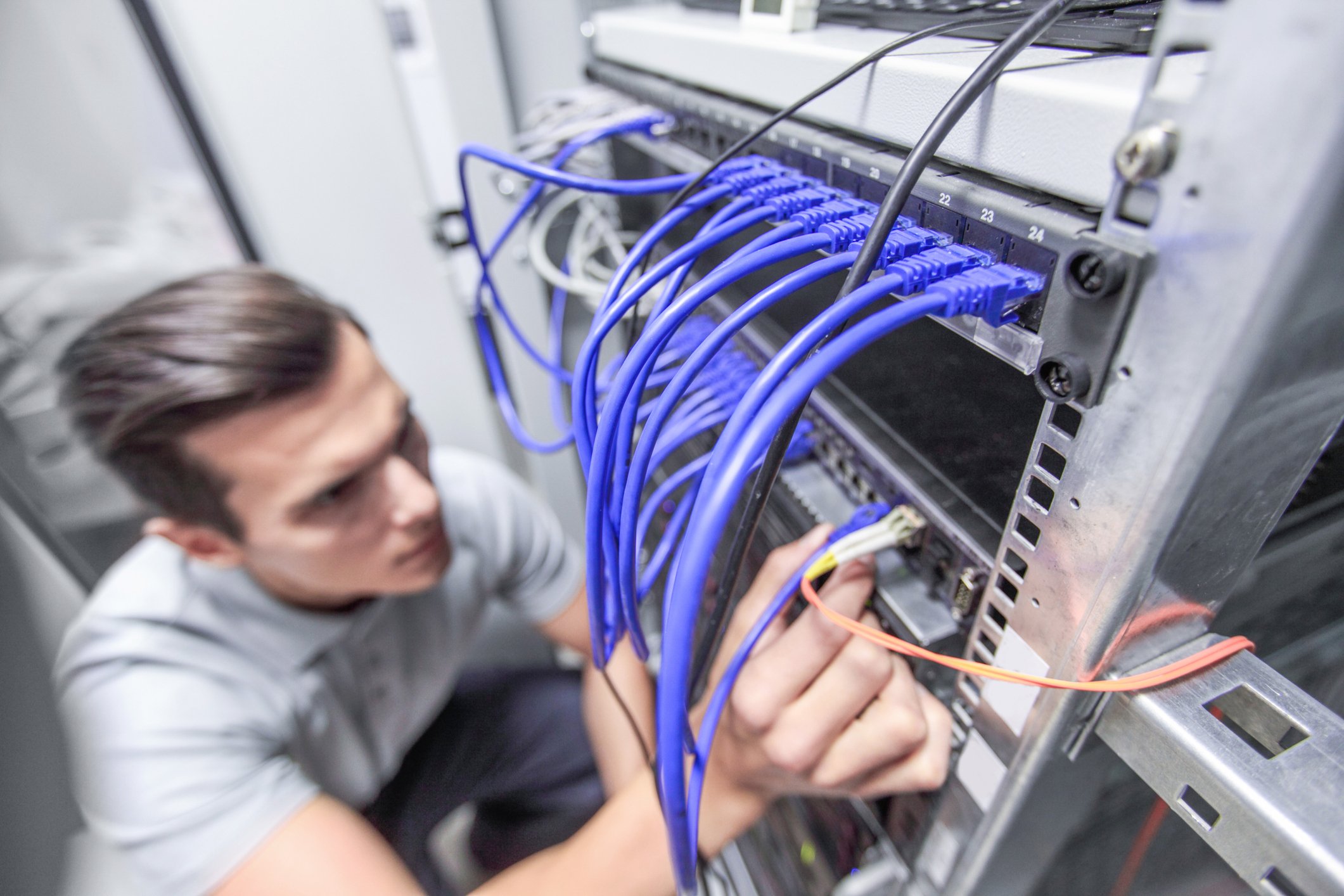 Man working in network server room plugging cables into the back of a rack of servers.
