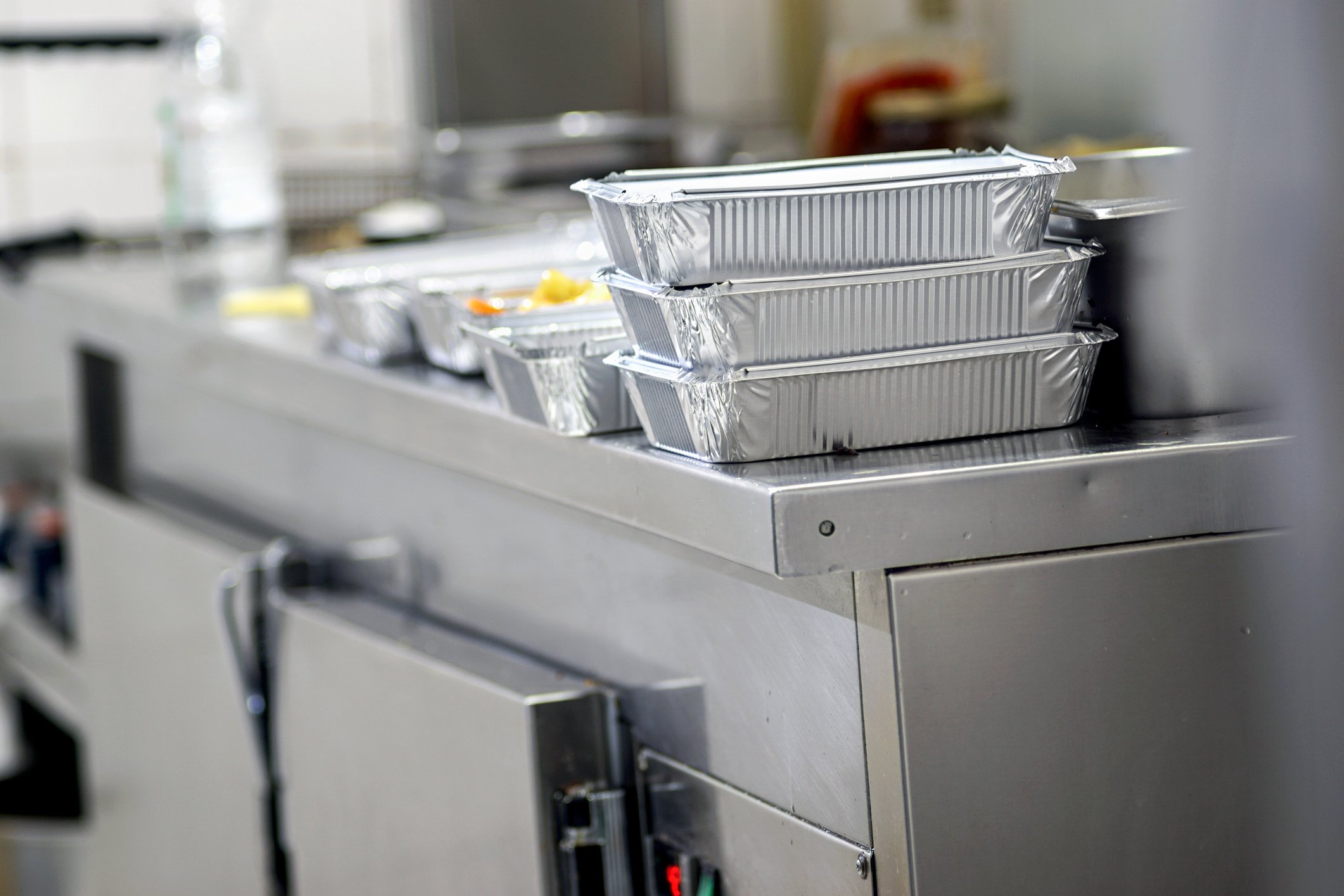 Multiple trays of food in takeout containers on a steel kitchen counter