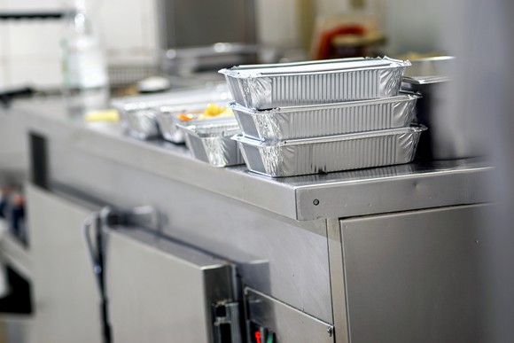 Multiple trays of food in takeout containers on a steel kitchen counter