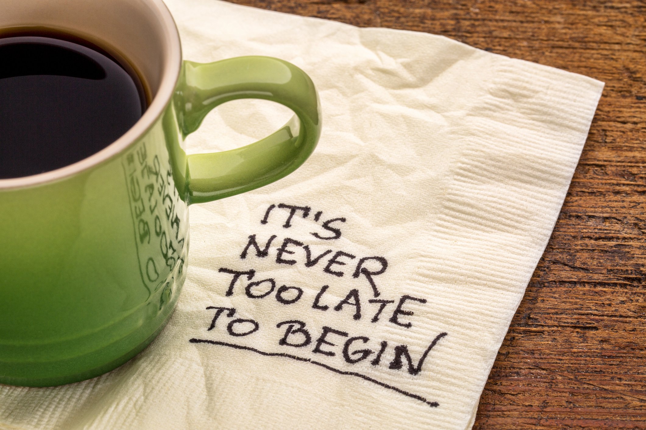Coffee cup sitting on napkin that reads It's never too late to begin