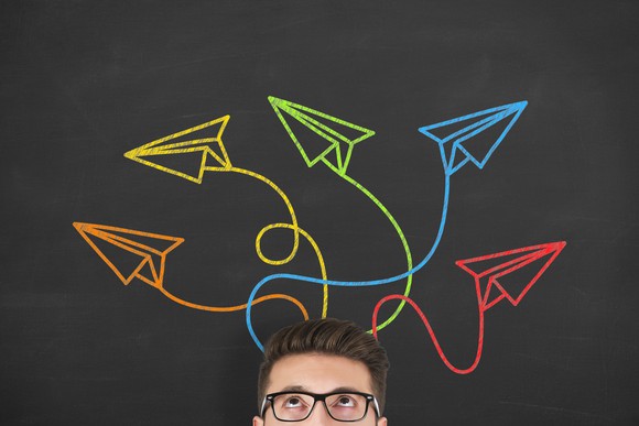A man looks up at several drawings of colorful paper planes flying around his head.