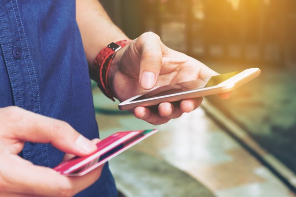 Man using smartphone while holding a credit card.