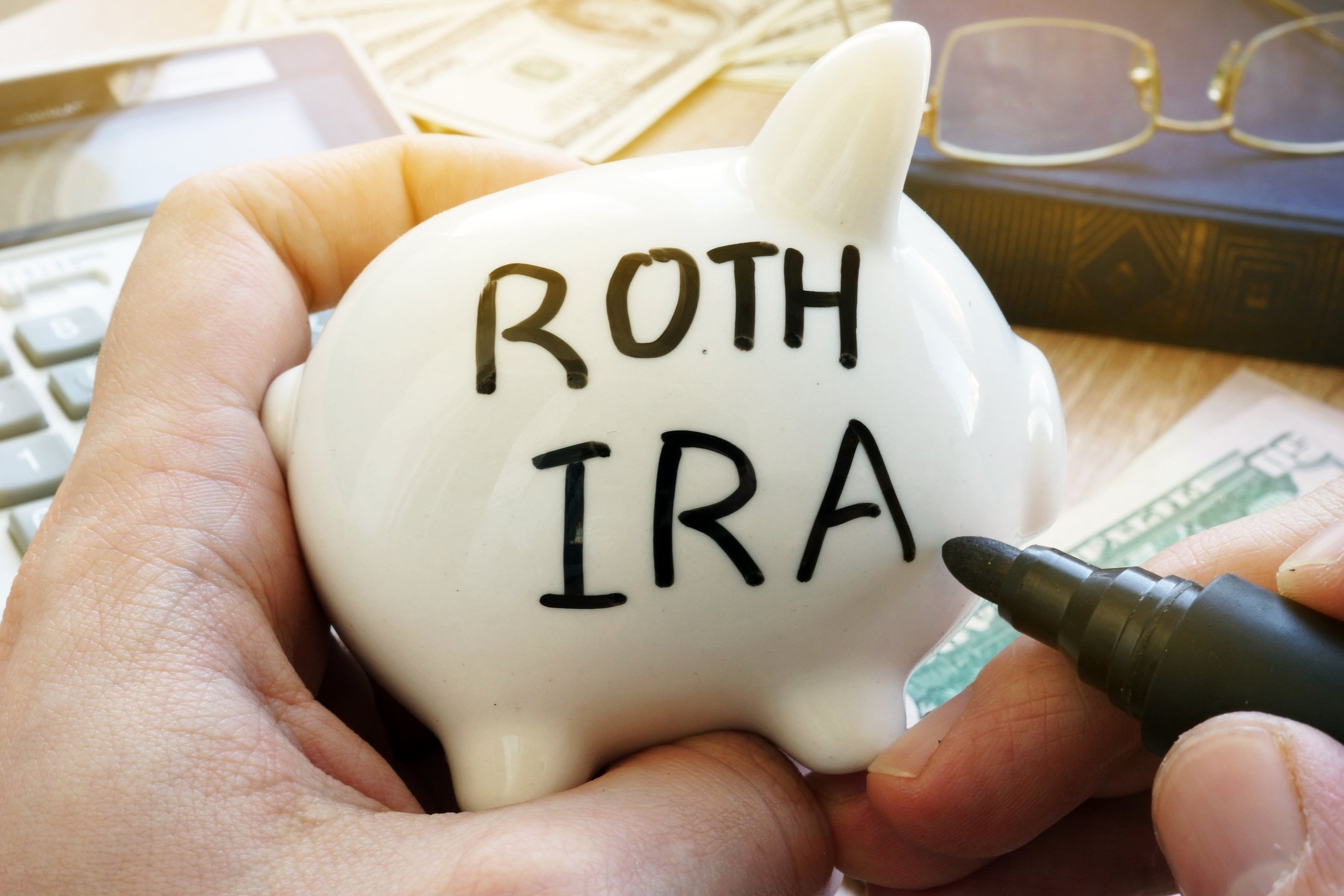 Someone writing Roth IRA on piggy bank