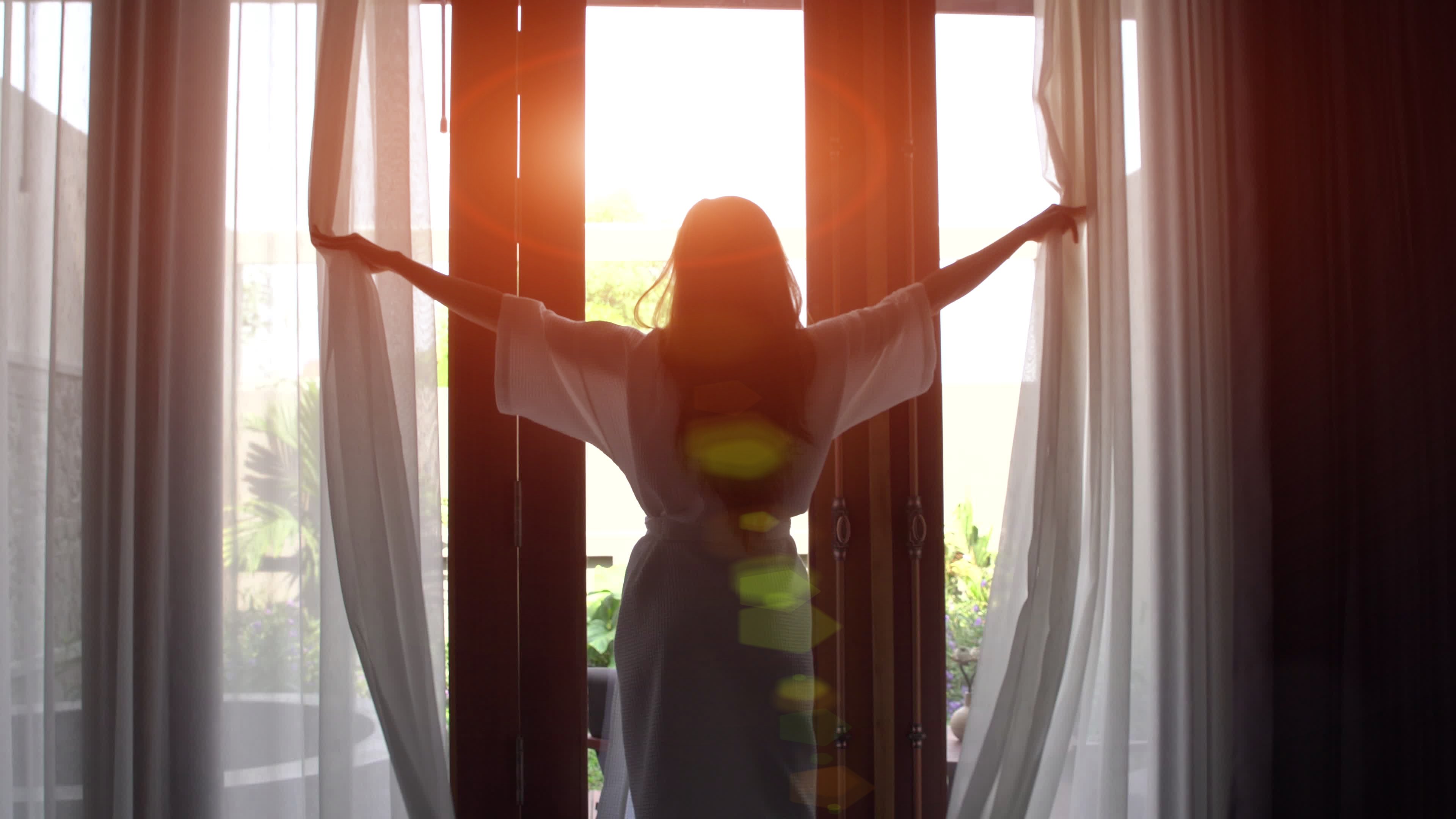 A woman throwing open the curtains of her hotel room.